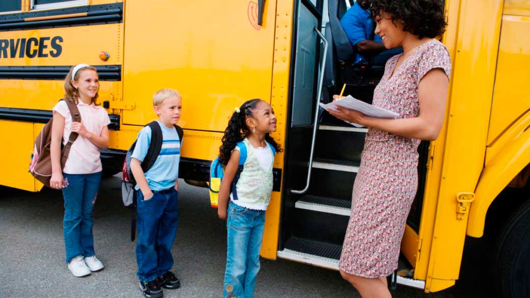 Female teacher taking a note of students before boarding school bus